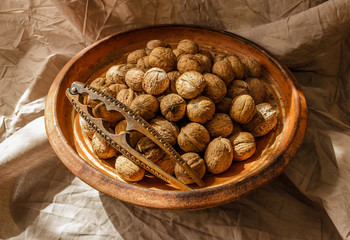 Whole walnuts in a vintage clay bowl and a nutcracker with sunlight