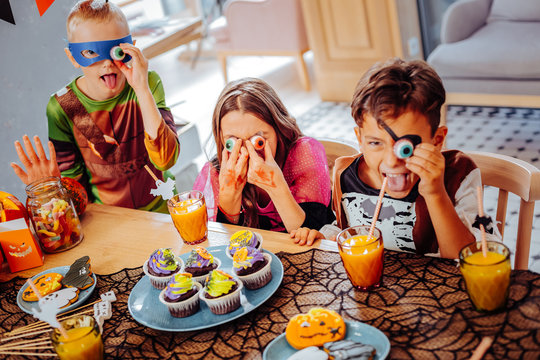 Halloween cookies. Three children wearing costumes having much fun while taking Halloween cookies in the form of eyes