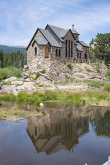 Fototapeta na wymiar Historic St Malo Roman Catholic Chapel is also called Chapel on a Rock and St. Catherine of Siena Chapel built in 1900's in Allenspark, Colorado. Saint Malo is reflected in the pond. 