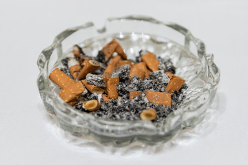 Cigarette stubs and ash in a glass ashtray. Isolated white background. Horizontal. side view