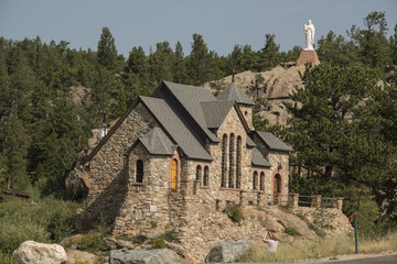 Historic St Malo Roman Catholic Chapel is also called Chapel on a Rock and St. Catherine of Siena Chapel, Allenspark, Colorado. Statue of Jesus Christ on hillside overlooking the chapel.