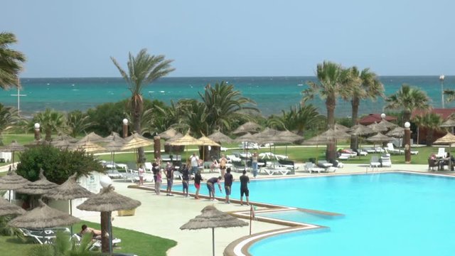 Beautiful tropical beach front hotel resort with swimming pool, sun-loungers and palm trees during a warm sunny day, paradise destination for vacations