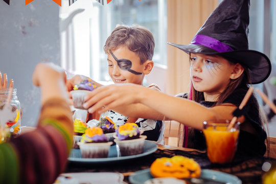 Thematic sweets. Children with painted faces celebrating Halloween at kindergarten feeling happy eating thematic sweets