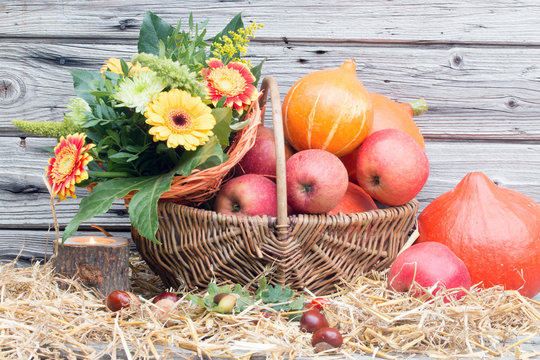 Herbstliche Dekoration mit Herbstblumen K&uuml;rbisse &Auml;pfel vor Holz rustikal auf Stroh