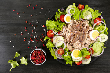 Salad with tuna, anchovies and vegetables. Mediterranean food. The background is black. Top view. Copy space. Horizontal shot.