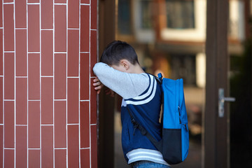 Schoolboy cries in the yard of the school leaning against the wall