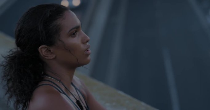 young hispanic woman runner resting exhausted after intense running exercise in city at sunrise training cardio female athlete wearing earphones listening to music close up