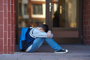 Schoolboy crying in the yard of the school - obrazy, fototapety, plakaty