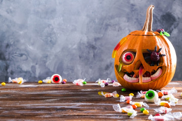 Orange pumpkin carved into Jack o Lantern with eyeball candy and gummy worms & spiders on wooden table. Background, copy space, close up, top view. Halloween party decoration. Trick or treat concept.