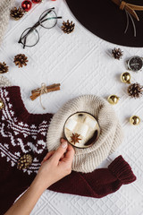 Winter concept. Flat lay view of bumps and tartan textured red sweater on white background with cup of coffee, glasses and a hat . 