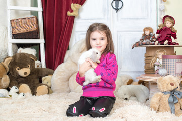 Happy laughing little girl playing with a baby rabbit, hugging her real bunny pet and learning to take care of an animal. background with toy bears