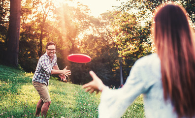 Happy couple playing frisbee in the park. Sport, recreation, lifestyle, love concept - obrazy, fototapety, plakaty