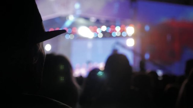 old man in a hat at . crowd at concert - summer music festival. Concert crowd attending a concert, people silhouettes are visible, backlit by stage lights. audience lifestyle watching the concert on