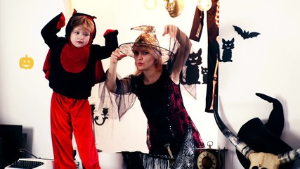 A woman in a suit of a witch and a little boy in a dragon suit scare everyone for a Halloween holiday. Happy family mother and son in costumes on a celebration of Halloween.