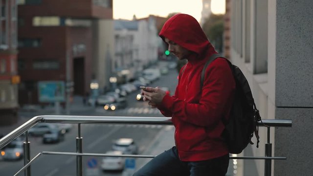 Young man in red jacket using smart phone in city, road on background