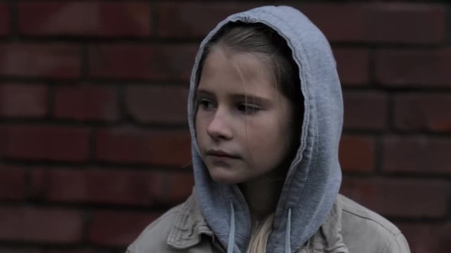 Refugee homeless child. Dark portrait of preteen girl standing in front of brick wall, she is looking unhappy and sad.