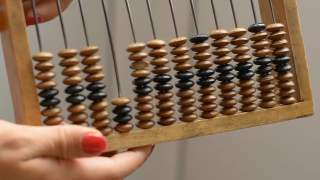 A girl is holding a vintage wooden abacus, performs a calculation on counter. Close-up.