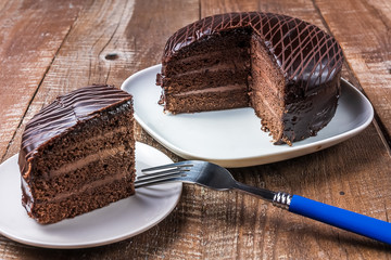 Delicious chocolate cake on a plate under wooden background.
