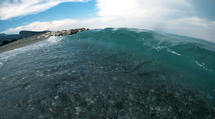 A sea wave near the shore with a piece of beach, mountains and stones