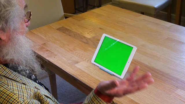 Older man with beard talking to tablet greenscreen