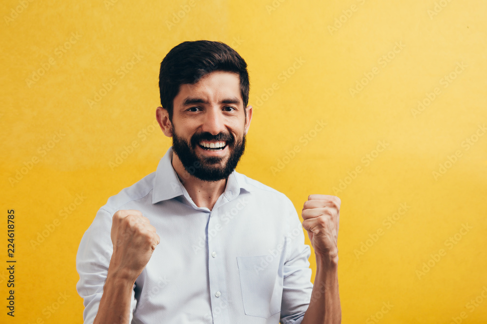 Wall mural Portrait of a satisfied young man celebrating isolated over yellow background