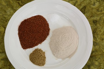 Three spices for enchilada sauce on a white plate sitting on a green table cloth