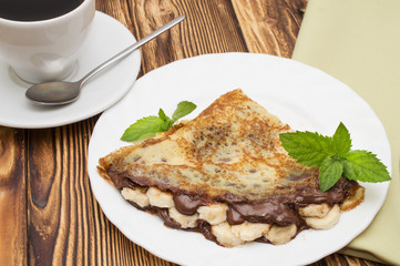 Crepes with bananas and cream on a wooden background