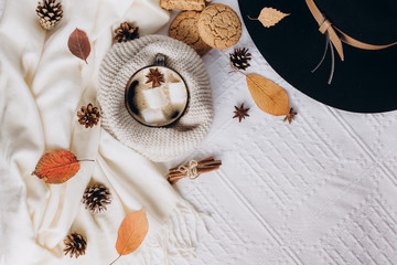 Autumn and Winter composition. Hot coffee with marshmallows, scarf, cookies, hat, bumps and autumn leaves. Flat lay, top view