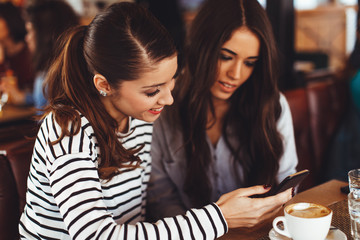 Two young women looking in smartphone screen in cafe