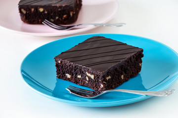Dark chocolate vegan brownie cake with nuts blue and pink plate white background. Selective focus.