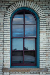 Brick wall with an arch reflecting the clouds in a window.