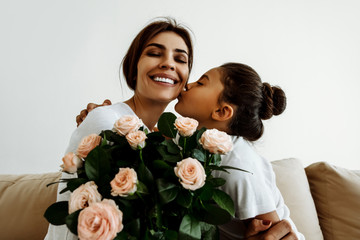 Family. Love. Holiday. Mom and daughter. Girl is giving a bouquet for her mother and kissing her, woman is smiling; at home - obrazy, fototapety, plakaty