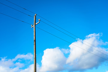 Wooden electric pole against a blue cloudy sky.       