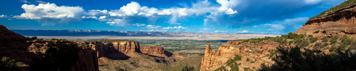 Ultra-wide panorama of the stone landmarks, plants, distant mountains, and vast sky of Colorado National Monument