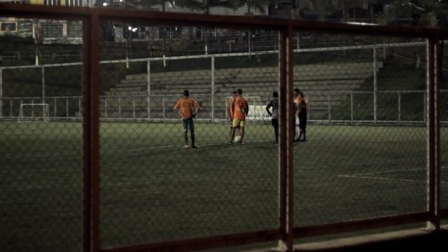 Young kids on a soccer team chatting around the ball on the field on a night training session, in Colombia