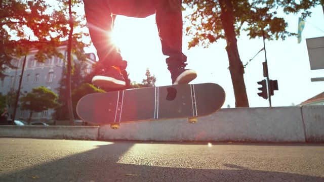 SLOW MOTION, CLOSE UP, LENS FLARE: Young man with long hair fails to land a trick with his skateboard. Caucasian skater dude slams to the concrete pavement after failing to do flip trick in sunny city