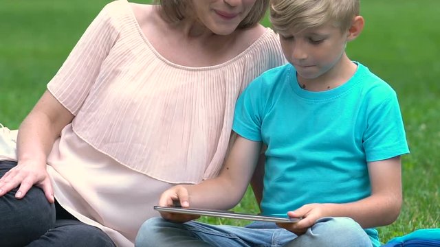 Pregnant mum playing game on tablet with son, happy motherhood, family planning