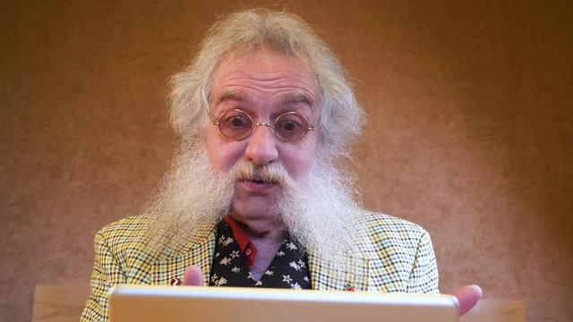 Older man with beard suprised from talking to someone over device