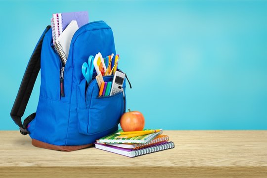 Colorful school supplies in backpack on blackboard