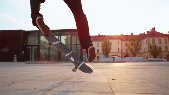 SLOW MOTION, CLOSE UP: Cinematic shot of male skater landing a fakie on sunny evening. Unrecognizable skateboarder jumps in the air and lands a cool trick while riding his board at beautiful sunrise.
