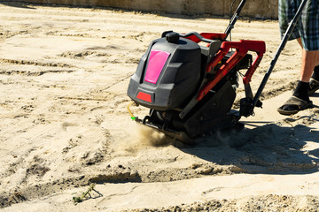 Builder with vibratory plates seals the base sand for pouring concrete.