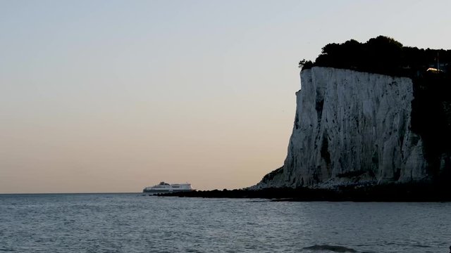 Sun-lit ferry passing behind dark shadowy Dover cliffs at evening at it approaches the ferry port at Dover, England