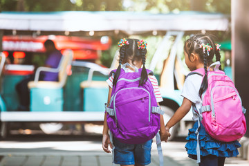 Asian pupil kids with backpack holding hand and going to school with school bus together. Back to school concept.