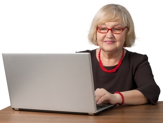 Friendly Old Woman Sitting behind Table and Typing on a Laptop -