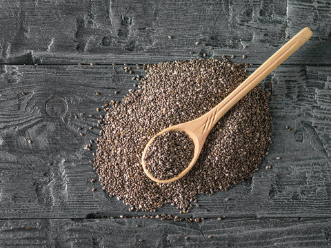 Wooden spoon on a pile of black Chia seeds. The view from the top. Flat lay.