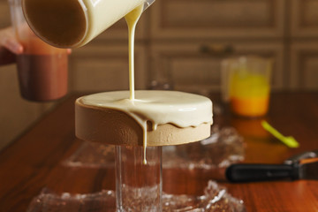 Cheesy mousse cake. Confectioner girl pours a delicate biscuit glaze. Master class in a home sweet shop. The glaze spreads on the cakes.