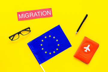 Schengen visa. Immigration to Europe concept. Text immigration near passport cover and european flag on yellow background top view