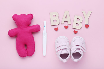 Pregnancy test with baby boots and soft toy on pink background