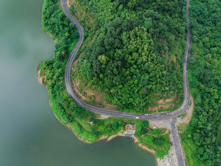 road in the middle of green forest in the rainy season on island with river lake aerial top view