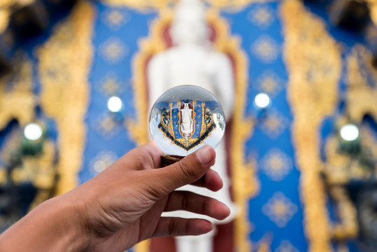 Crop hand of tourist holding glass ball with upside reflection of ancient temple in Thailand